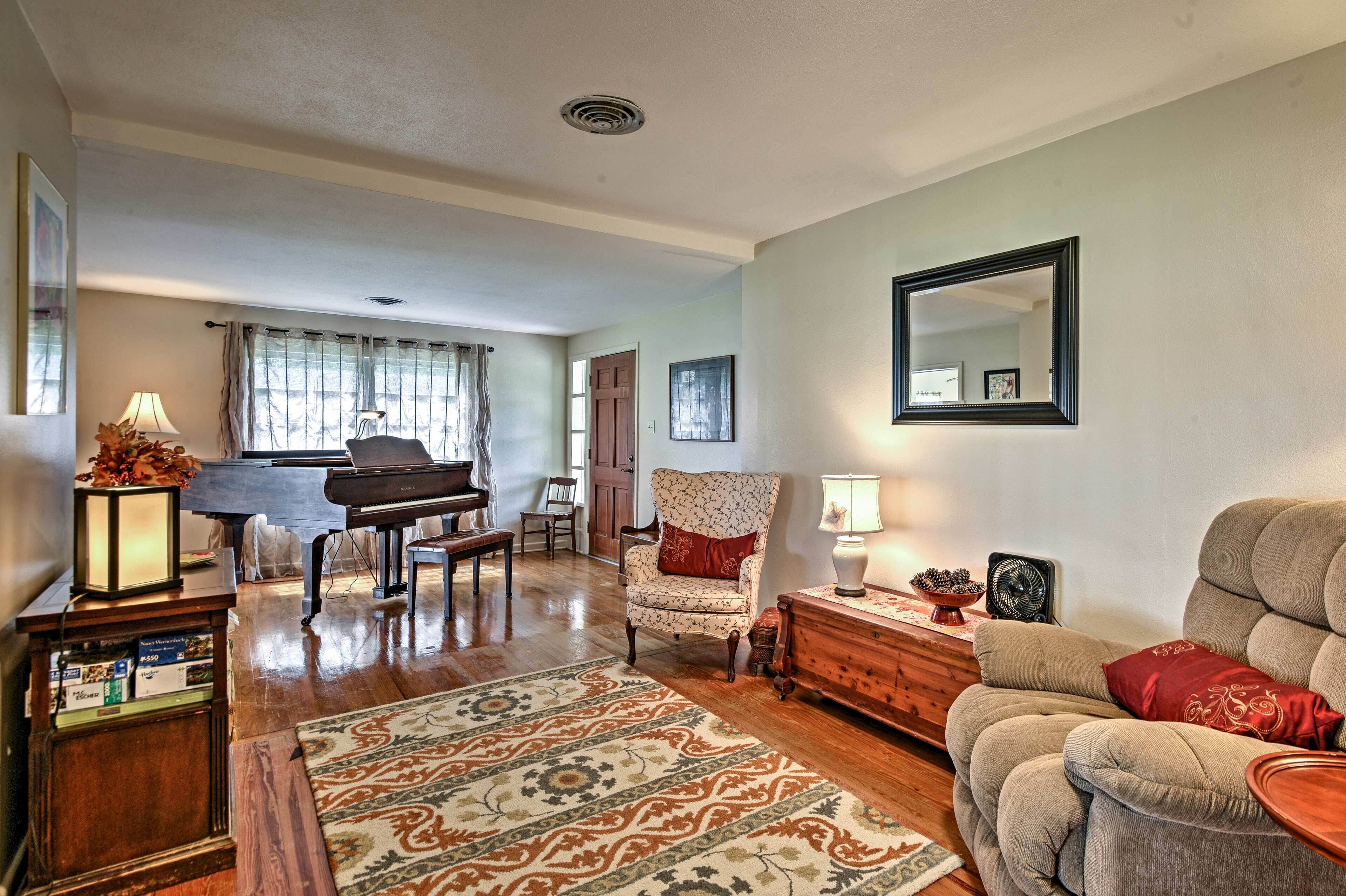 A spacious living room with a grand piano, a comfortable sofa, a patterned rug, and a wooden cabinet.