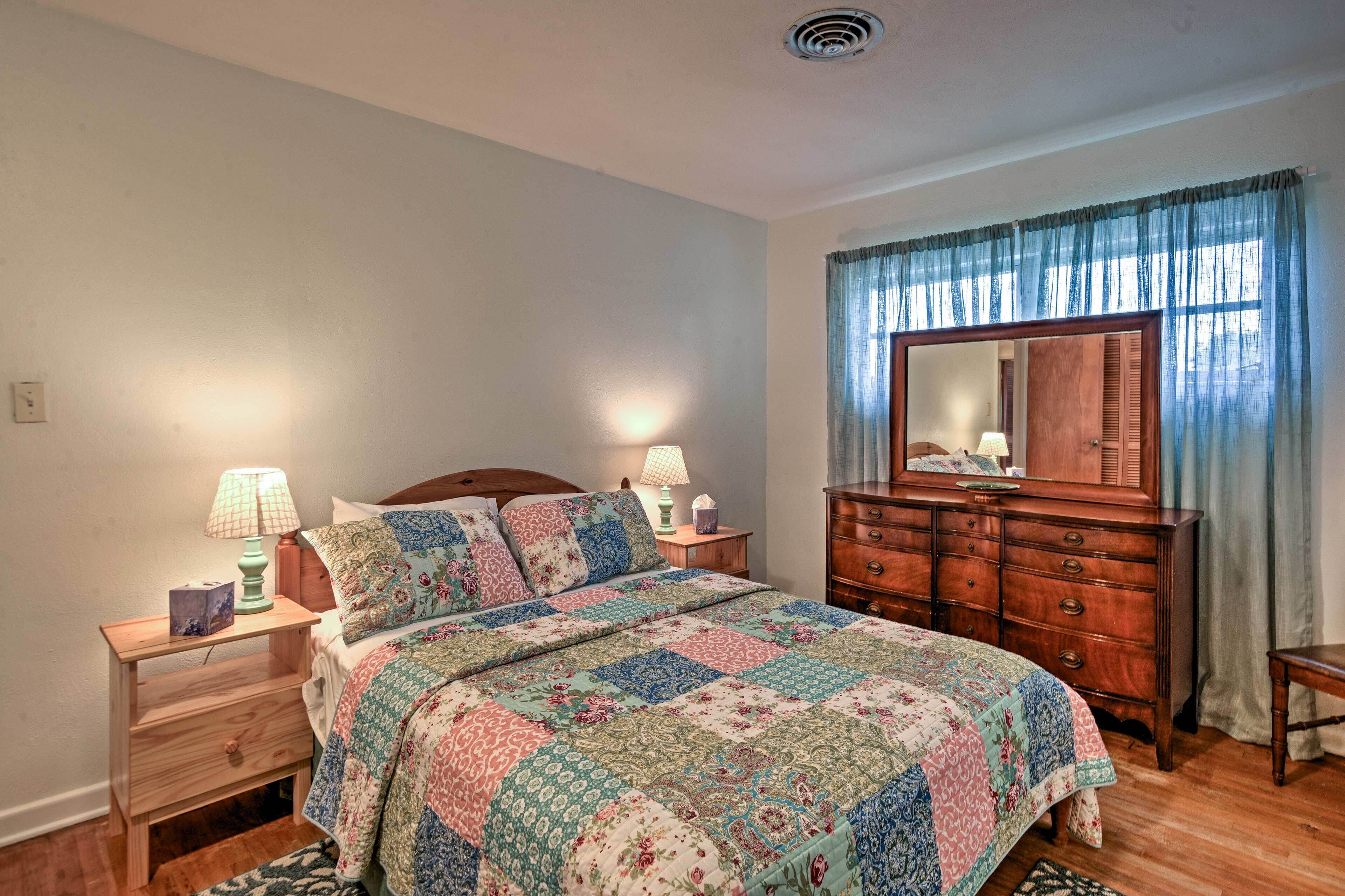 Une chambre à coucher avec une commode en bois, un lit recouvert d’une courtepointe, deux lampes de chevet, une table de chevet et un miroir au-dessus de la commode.