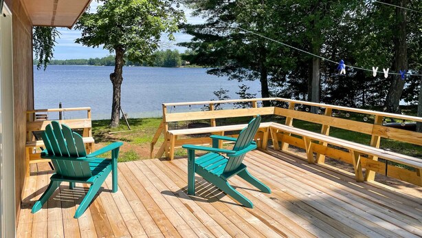 A wooden deck with two green Adirondack chairs facing a lake. - Lakefront Mercer Home: Private Dock & Kayaks! (Mercer)