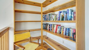 Una estantería de madera con varios estantes, una silla amarilla y diferentes libros.