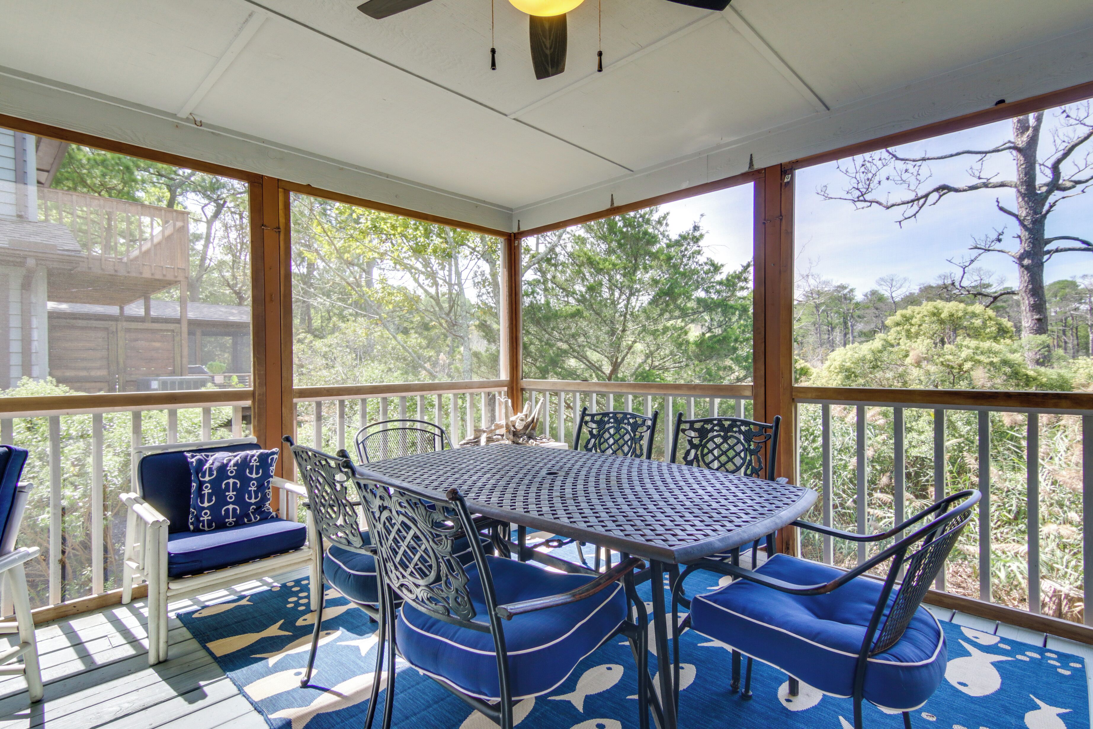 A covered outdoor patio with a round table and chairs, a sofa, and a view of the surrounding trees.