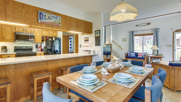 Una cocina con armarios de madera, una isla central y una zona de comedor con sillas azules y una mesa dispuesta para seis personas.