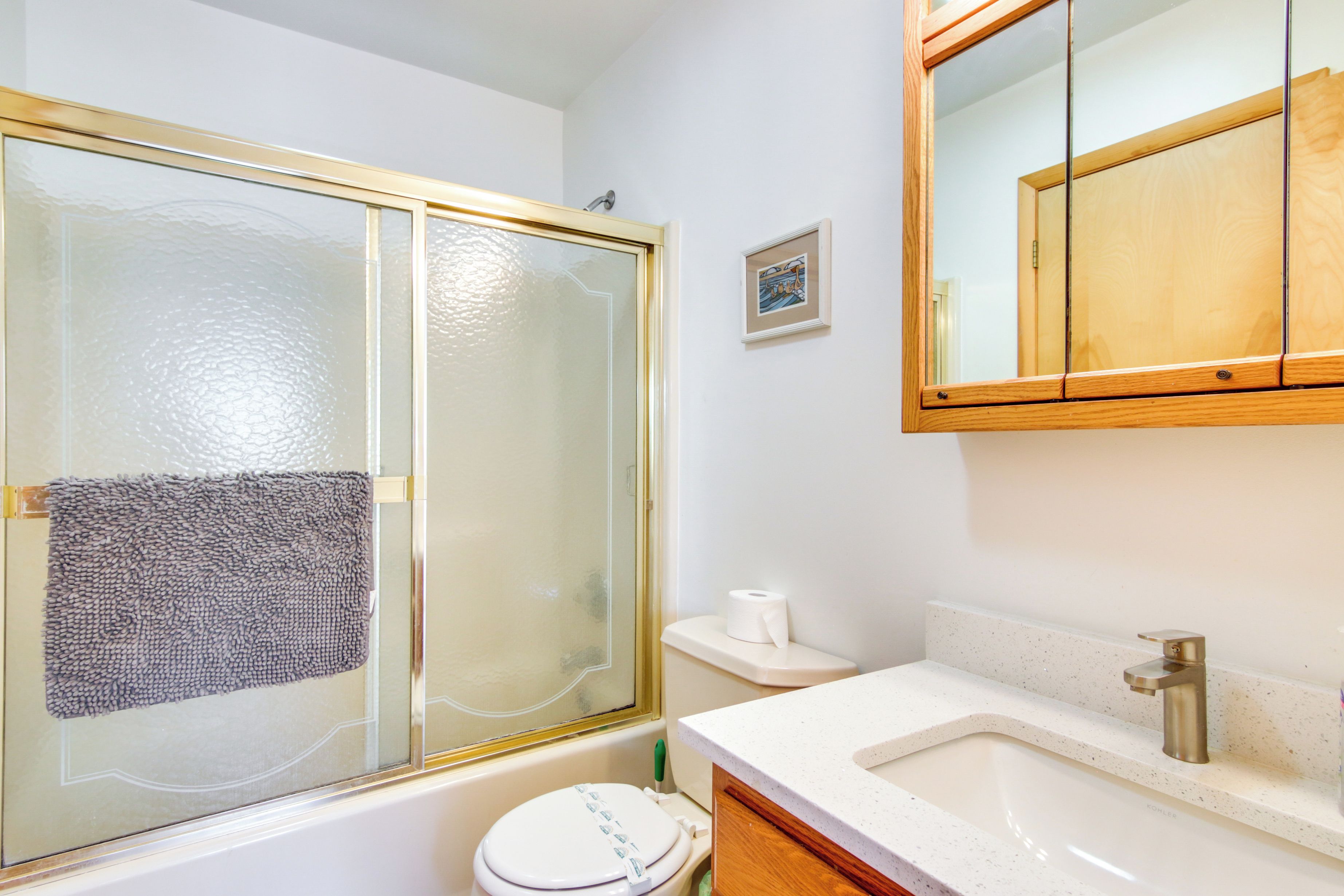 A bathroom with a glass-enclosed shower, a toilet, a sink with a mirror above, and a small framed picture on the wall.