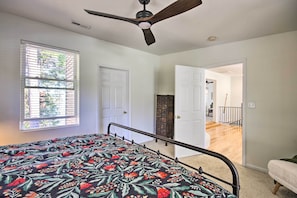 A bedroom with a bed, a ceiling fan, a window with blinds, and a door leading to another room.