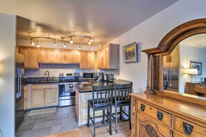 Una cocina moderna con armarios de madera, una isla central con sillas, electrodomésticos de acero inoxidable y un espejo grande sobre la isla.