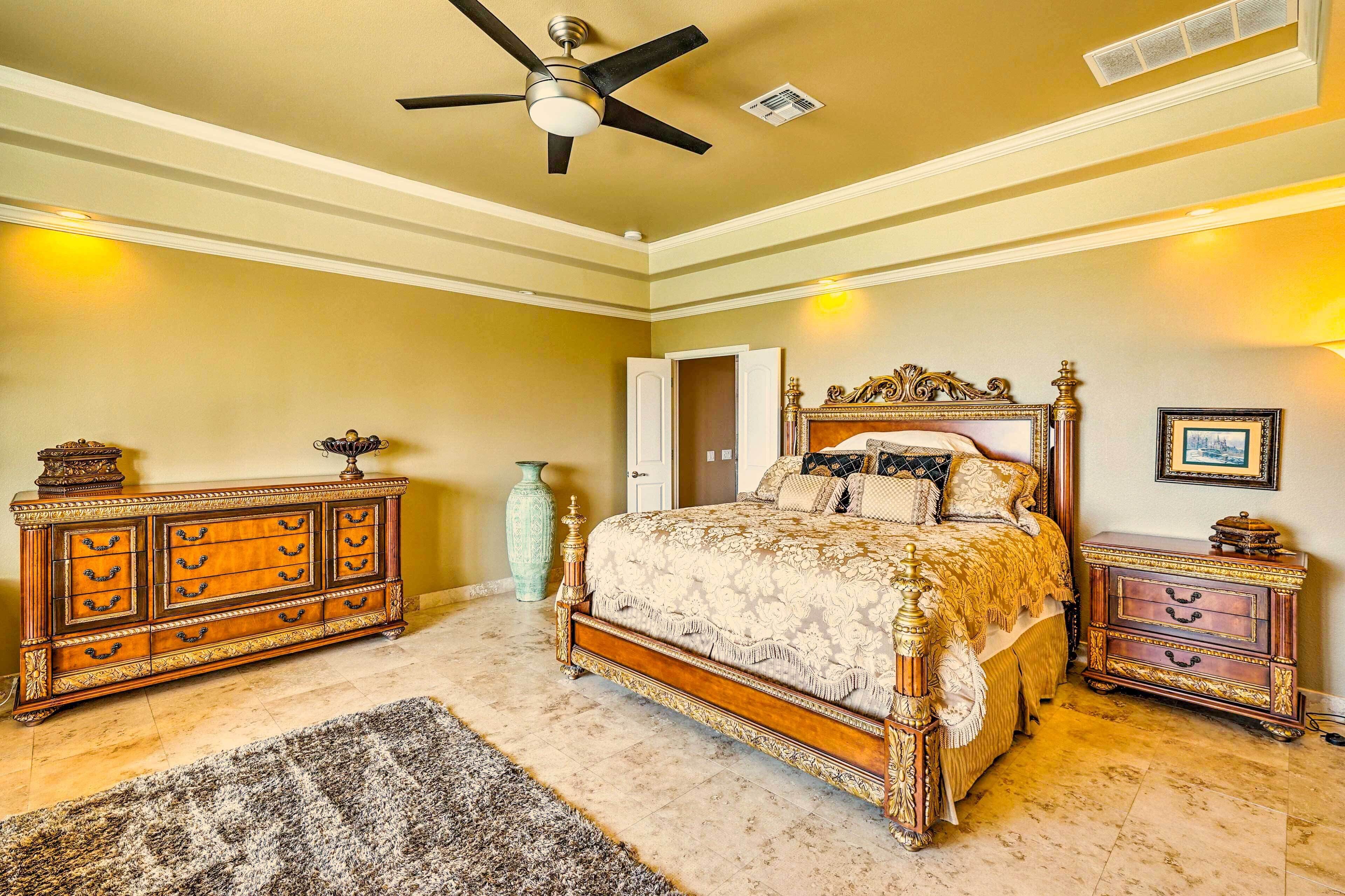 A bedroom with a large bed, a ceiling fan, a dresser, and a nightstand.