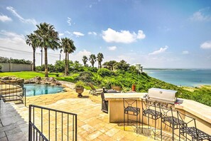A patio with a pool, outdoor grill, and seating area overlooking a scenic view of the ocean.
