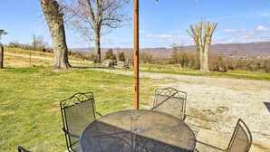 A patio with a round table and metal chairs, surrounded by trees and a clear view of distant mountains.