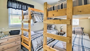 A bunk bed room with wooden frames, a dresser, and a window with blinds.