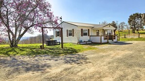A single-story house with a porch, a bench, and a tree with pink blossoms.