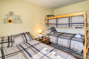 A room with two beds, one with a bunk bed and the other with two single beds, all with plaid bedding. There is a small table with a lamp and a decorative item on it.