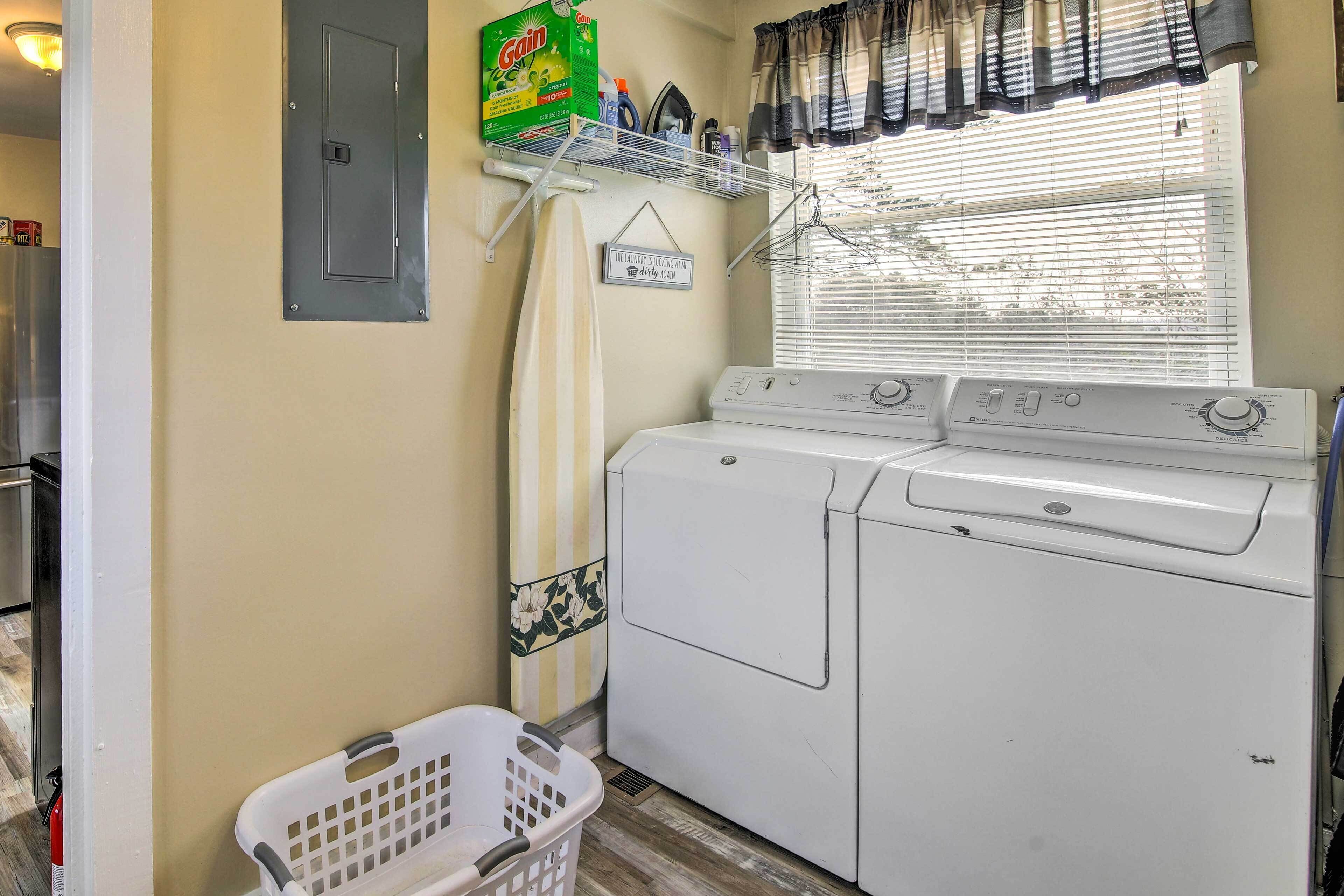 A laundry area with a washing machine, a dryer, a shelf with laundry supplies, and a basket.