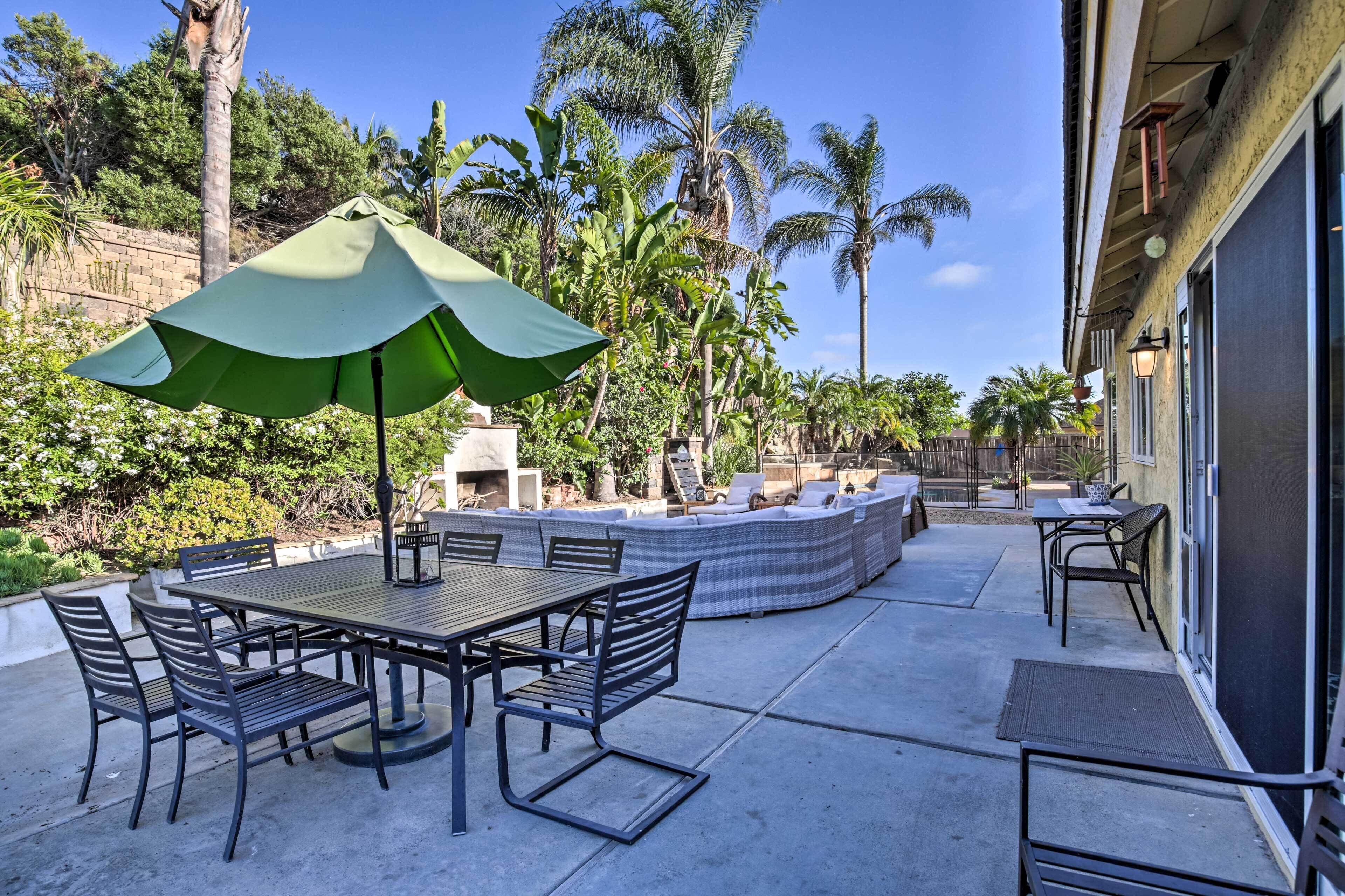 Um pátio externo com mesa, cadeiras e um guarda-sol verde.