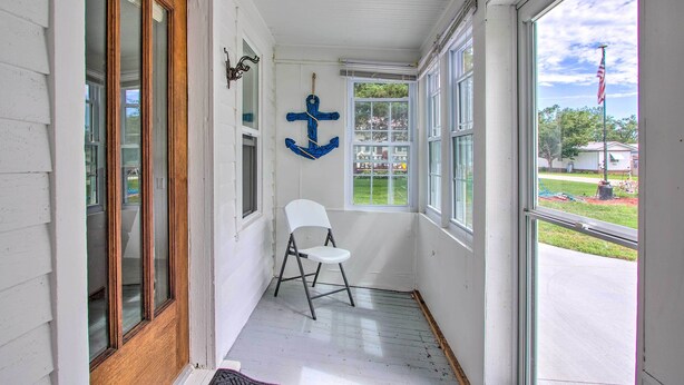 Un porche estrecho con una silla blanca, una puerta de madera y un ventanal grande.