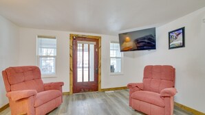 Una habitación con dos sillones rosados, una puerta de madera y un televisor montado en la pared.