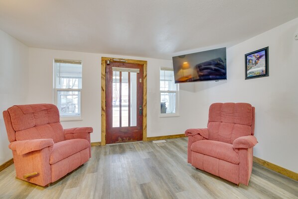 A room with two pink armchairs, a wooden door, and a television mounted on the wall.