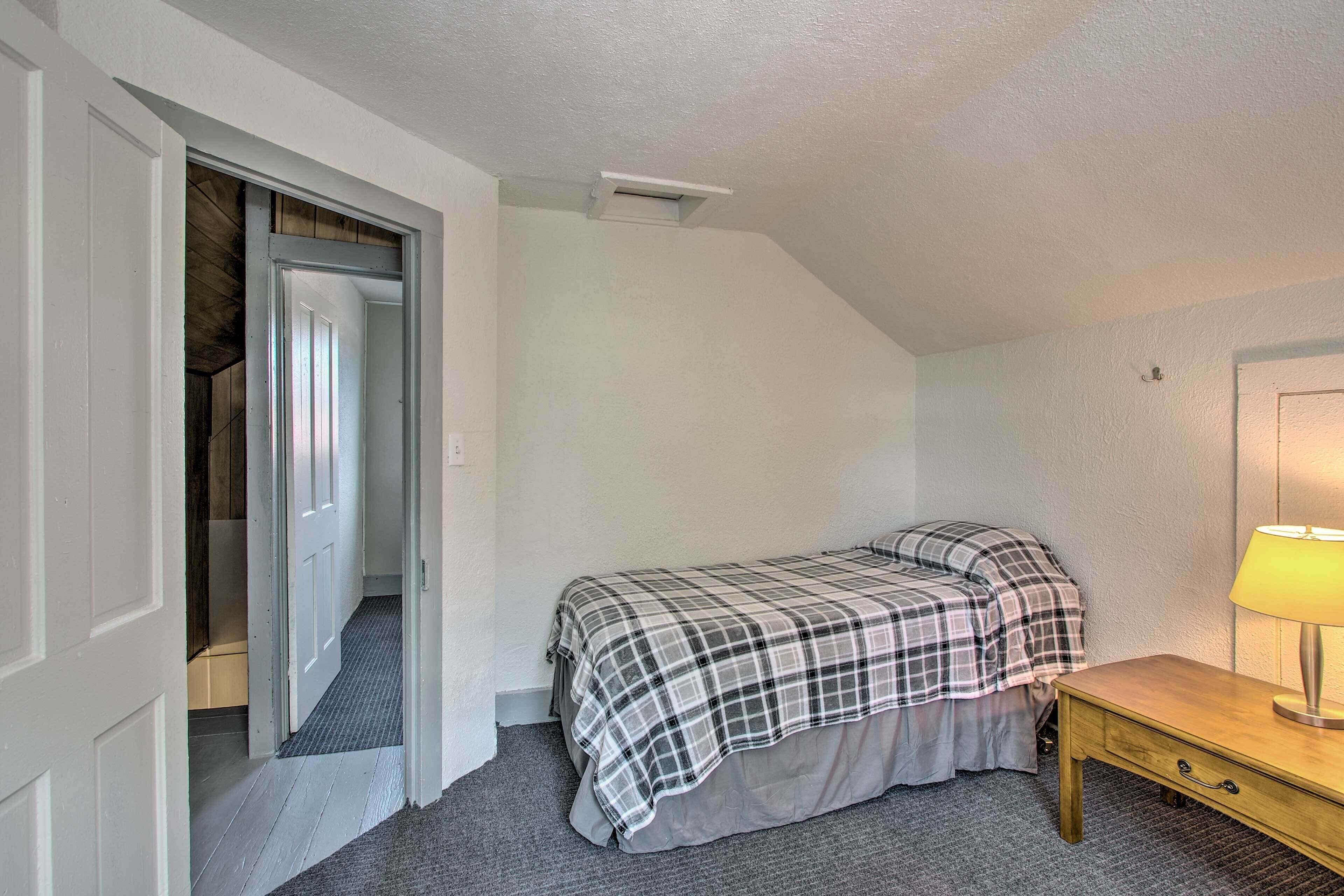 A bedroom with a bed, a bedside table with a lamp, and a door leading to another room.
