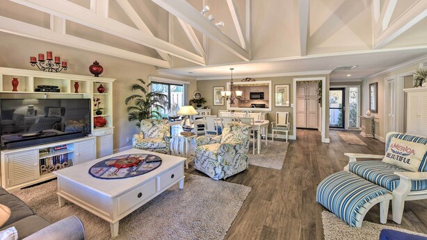 A spacious living room with a large television, comfortable seating, and a kitchen area in the background.