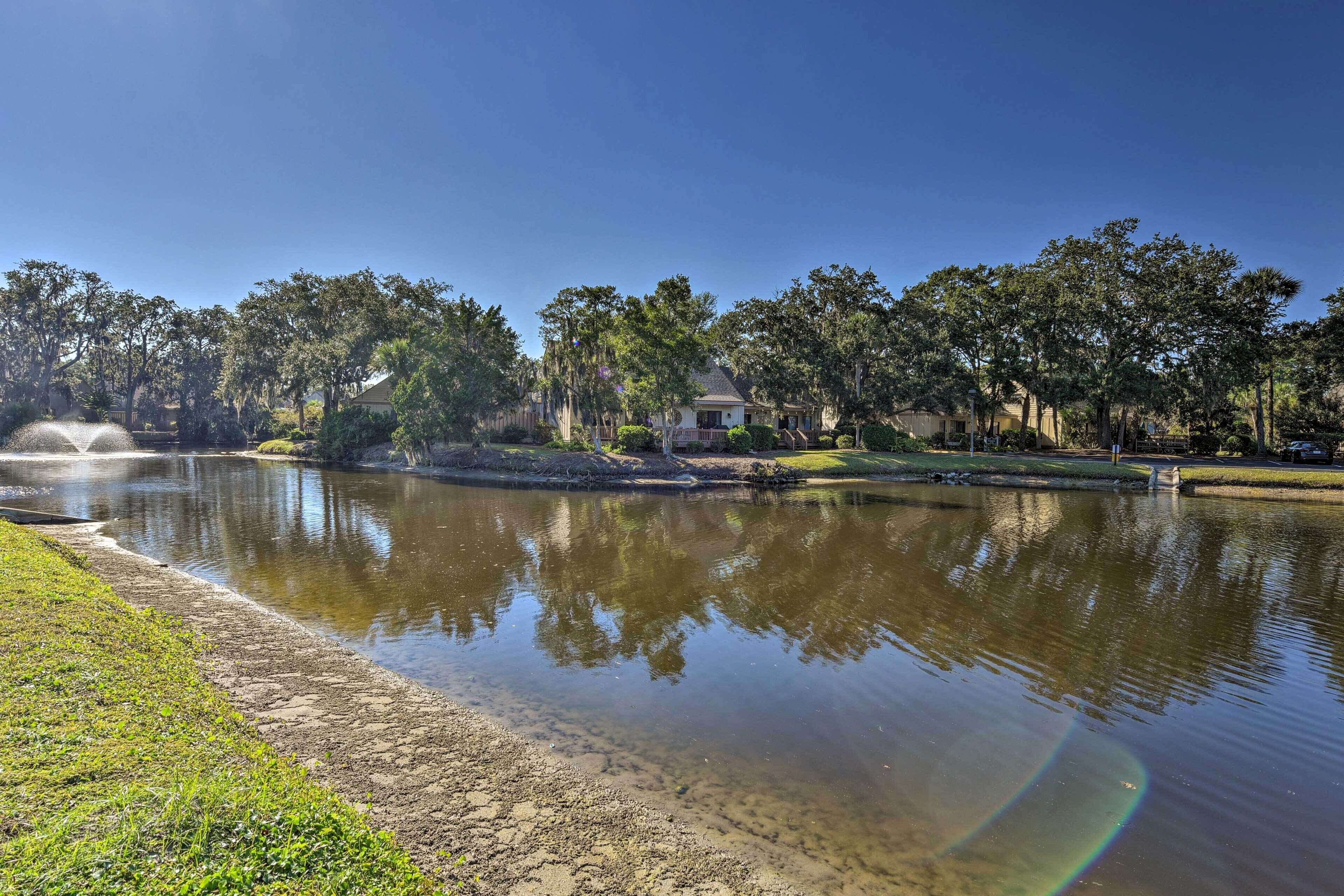 Un lago tranquilo con reflejos nítidos, rodeado de árboles y una casa al fondo.
