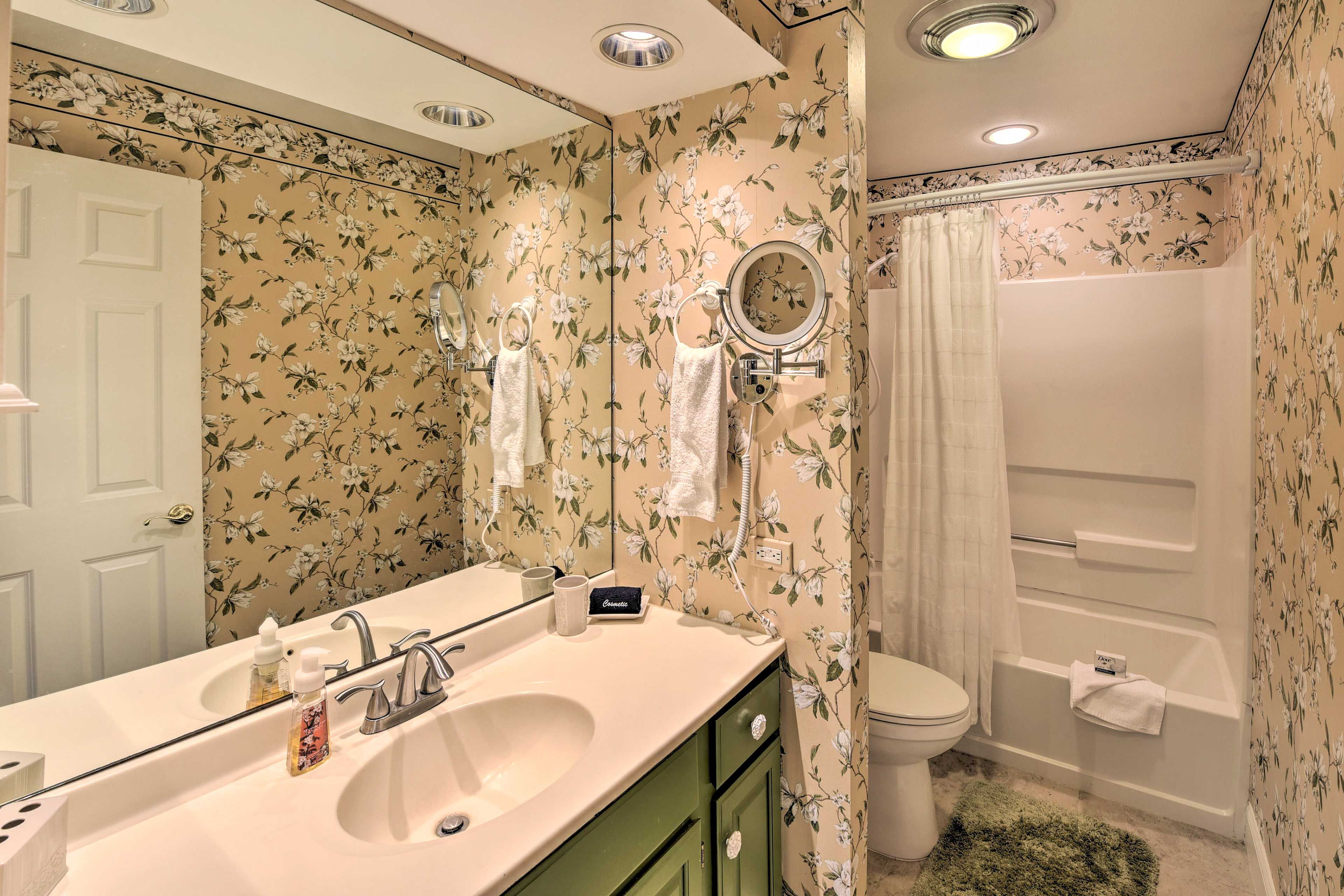 A bathroom with floral wallpaper, a double sink, a mirror, a toilet, and a bathtub.