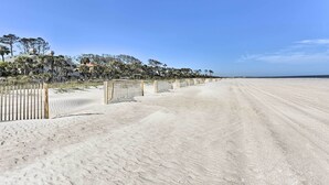 A sandy beach with a wooden fence and a row of trees in the background.