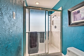 A modern bathroom with a glass-enclosed shower, a white toilet, and a teal textured wall. - Arkansas Retreat Near Lake Hamilton w/ Pool Access (Hot Springs)