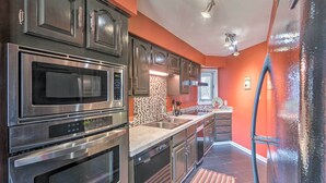 A modern kitchen with stainless steel appliances, a tiled backsplash, and a red accent wall. - Arkansas Retreat Near Lake Hamilton w/ Pool Access (Hot Springs)