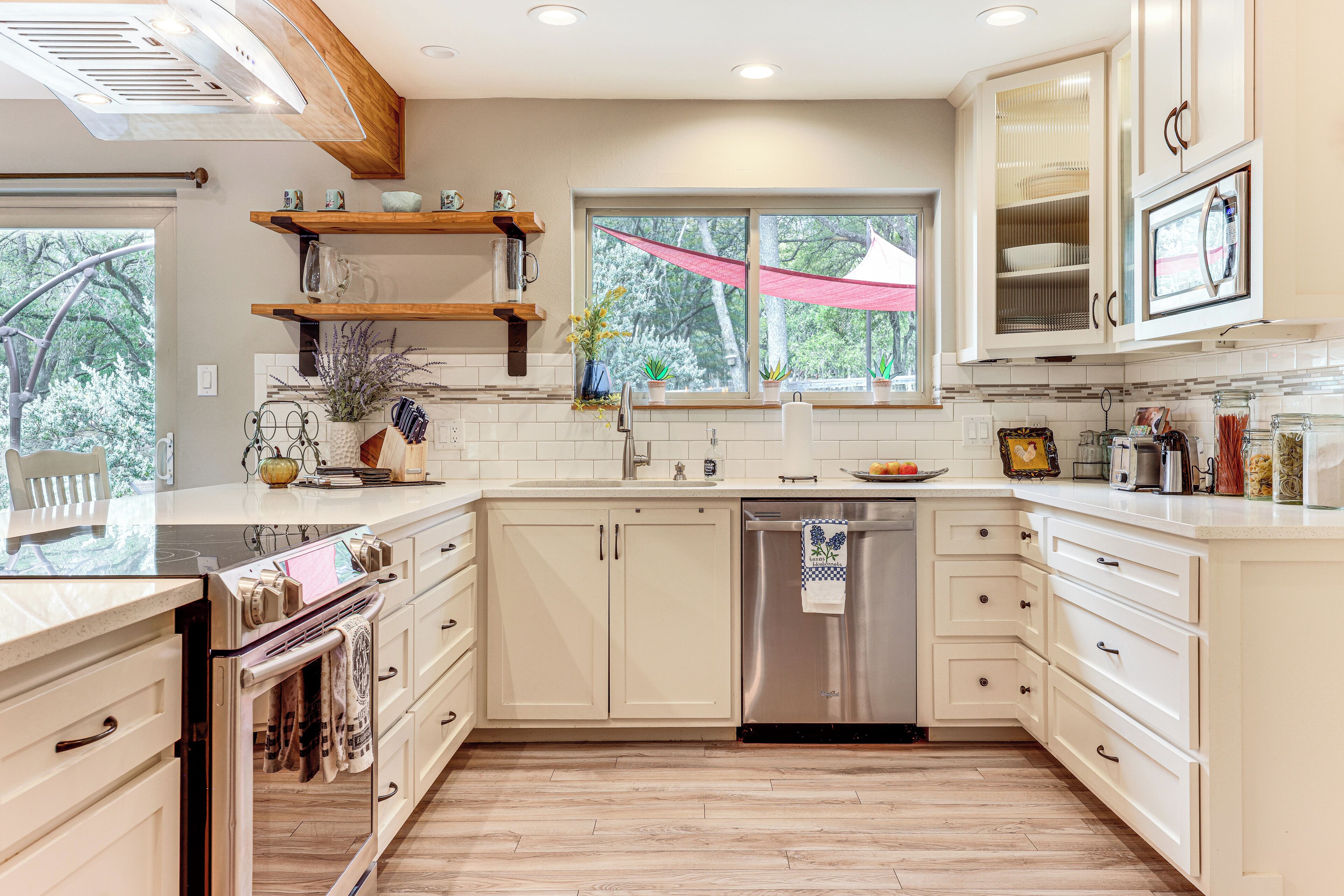 A modern kitchen with white cabinetry, a stainless steel dishwasher, and a wooden countertop.