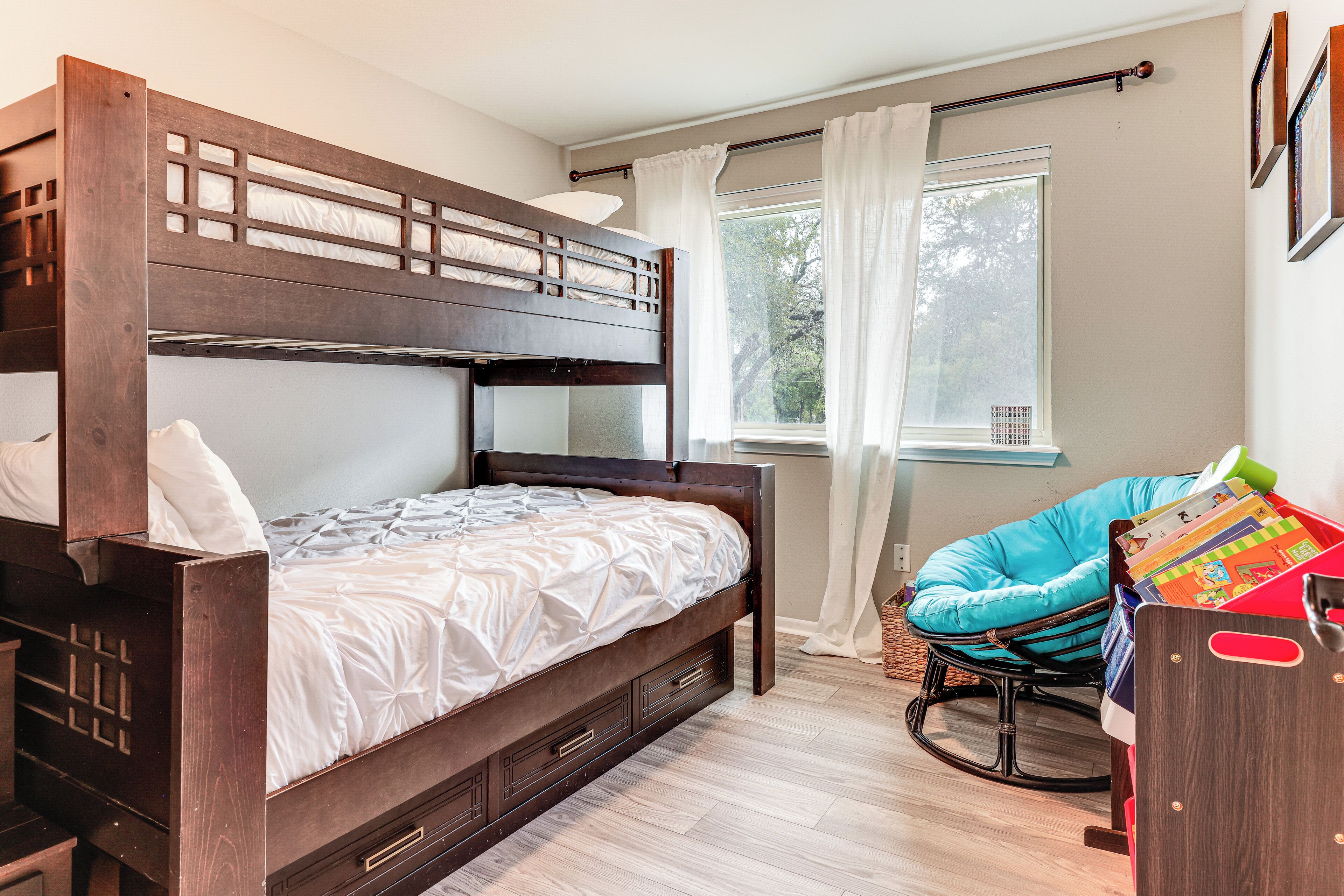 A bunk bed with a wooden frame and drawers, a rocking chair, and a window with curtains.