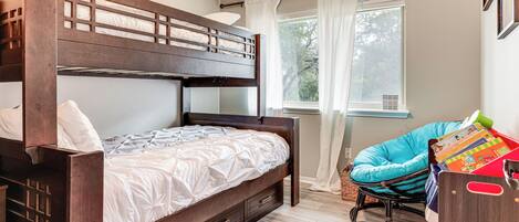 A bunk bed with a wooden frame and drawers, a rocking chair, and a window with curtains.