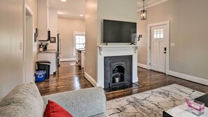 Una sala de estar con chimenea, televisor y una cocina al fondo.