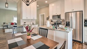 Una cocina moderna con armarios blancos, electrodomésticos de acero inoxidable y un comedor con una mesa y sillas de madera.