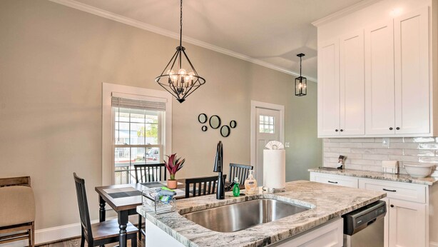 Una cocina moderna con una isla central, pileta de acero inoxidable, muebles color blanco y un candelabro.