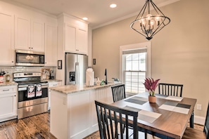 A modern kitchen with white cabinetry, stainless steel appliances, and a wooden dining table with chairs. - Ideally Located 'penne Place' w/ Deck & Grill (Greenville)