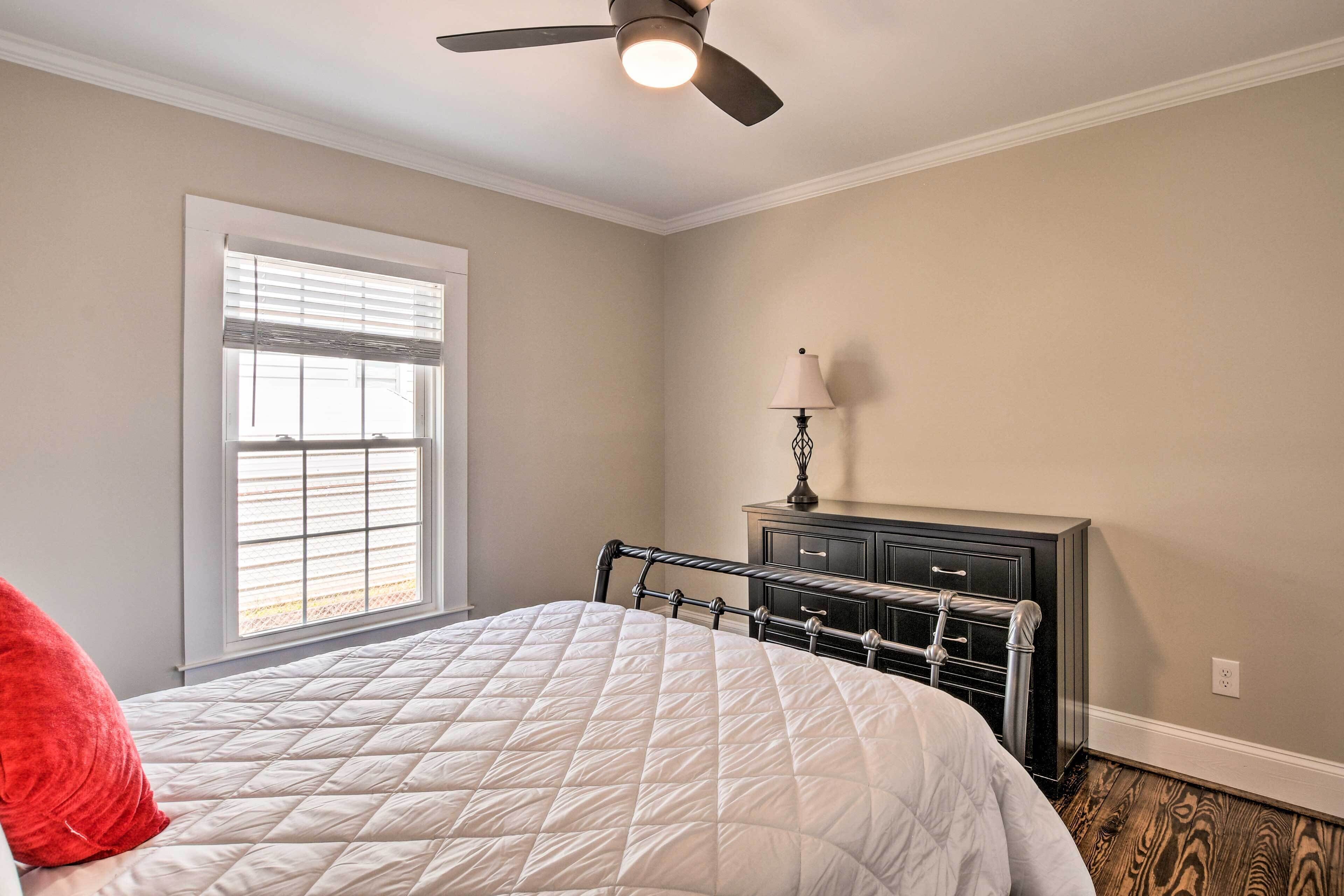 Un dormitorio con cama, ventilador de techo, cómoda y ventana con persianas.