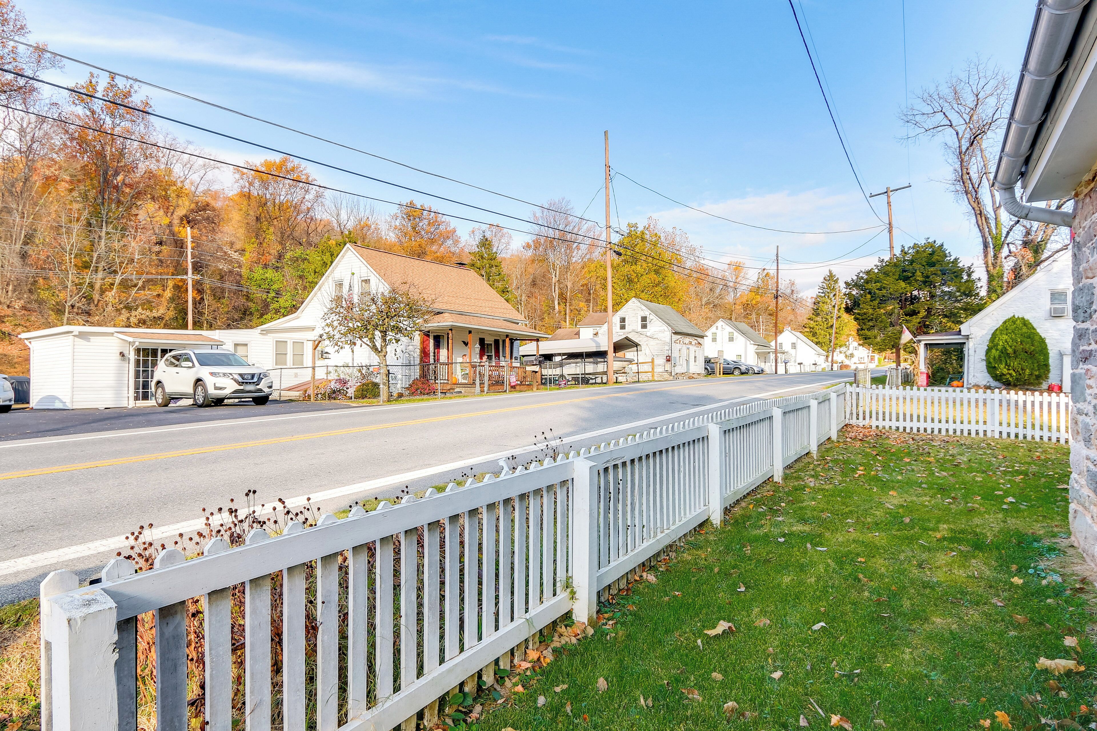 A residential street with houses, a white picket fence, and a grassy area.