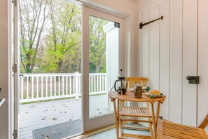 A wooden chair and table with a coffee pot and croissant on the table, a door with a view of a deck and trees, and a security camera mounted on the wall. - Historical Thurmont Escape w/ Furnished Deck! (Thurmont)