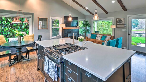 A spacious kitchen with a central island, wooden flooring, pendant lighting, and a view of a lush garden.