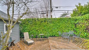 A wooden deck with outdoor furniture, a hedge wall, and a house in the background.