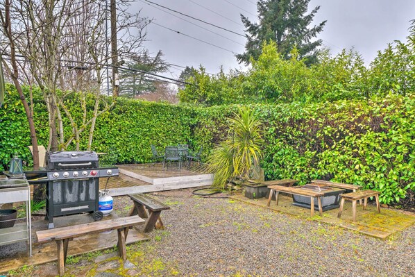 A backyard with a barbecue grill, picnic tables, and a small deck area.