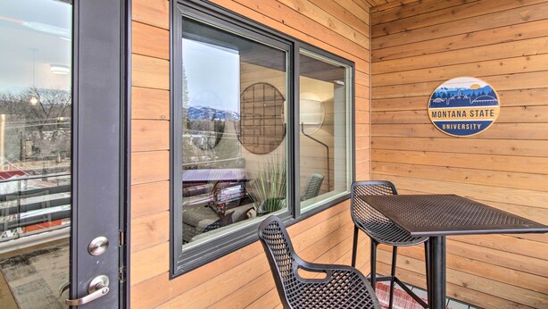 A wooden-paneled room with a large window, a table, and two chairs. A sign with "Montana State University" is visible. - Chic Bozeman Apartment - 1 Block Off West Main St! (Bozeman)