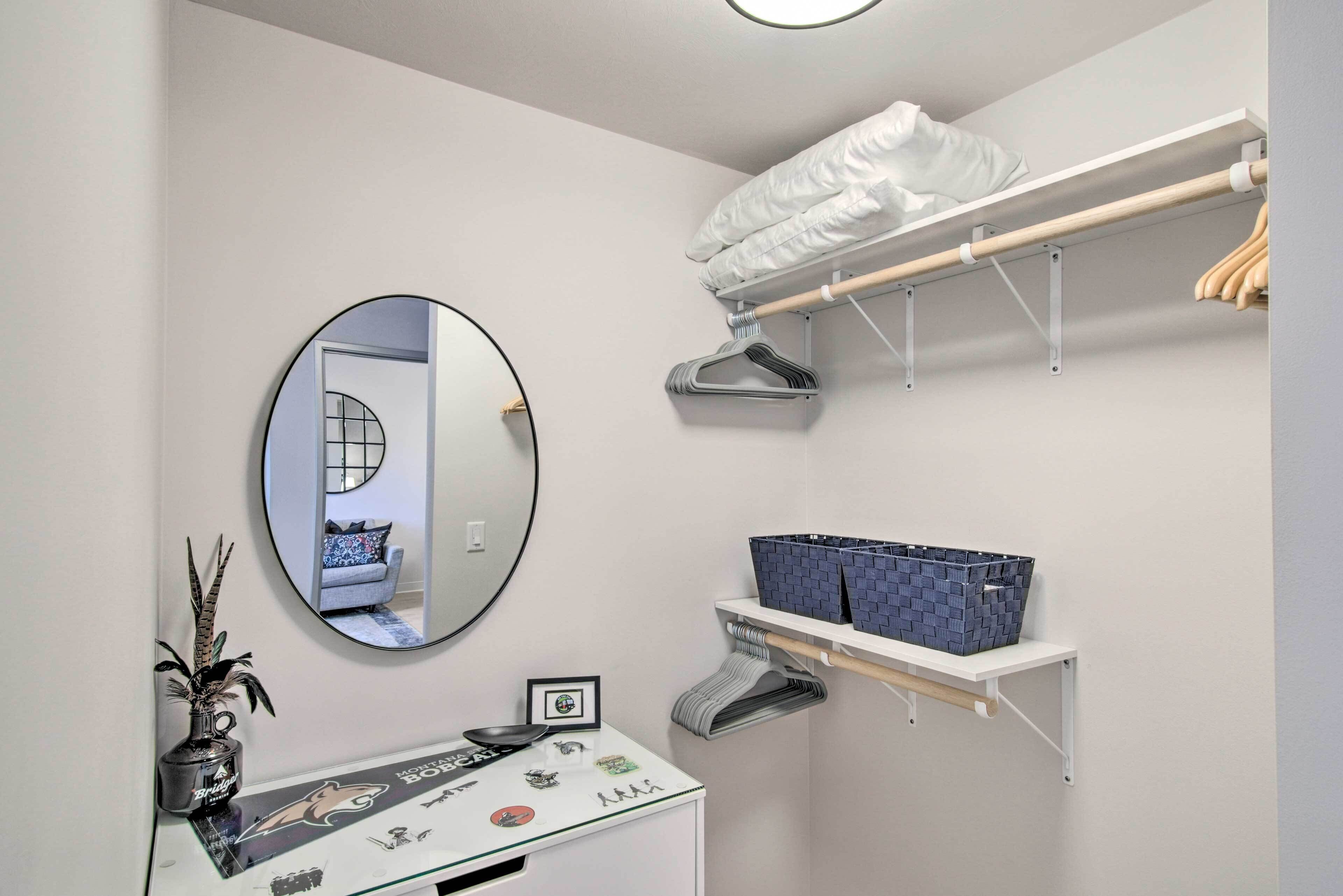A compact bathroom with a round mirror, a small vanity with a glass top, a towel rack, and a shelf with baskets.