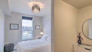 A bedroom with a bed, a nightstand, a lamp, a small stool, a window with a view, and a mirror on the wall. - Chic Bozeman Apartment - 1 Block Off West Main St! (Bozeman)