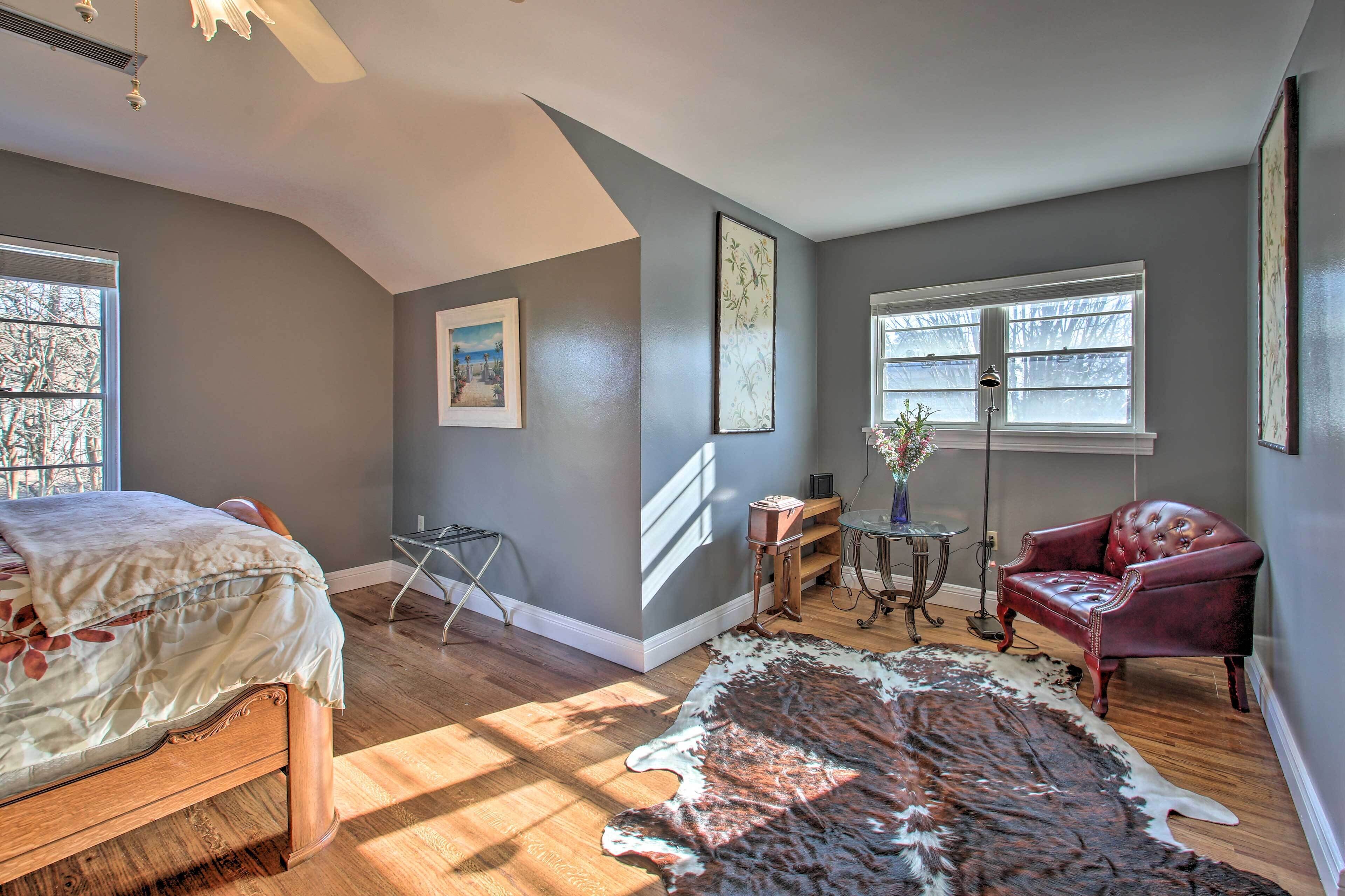 Een slaapkamer met een bed, een rode leren fauteuil, een groot vloerkleed en een bureau met een lamp.