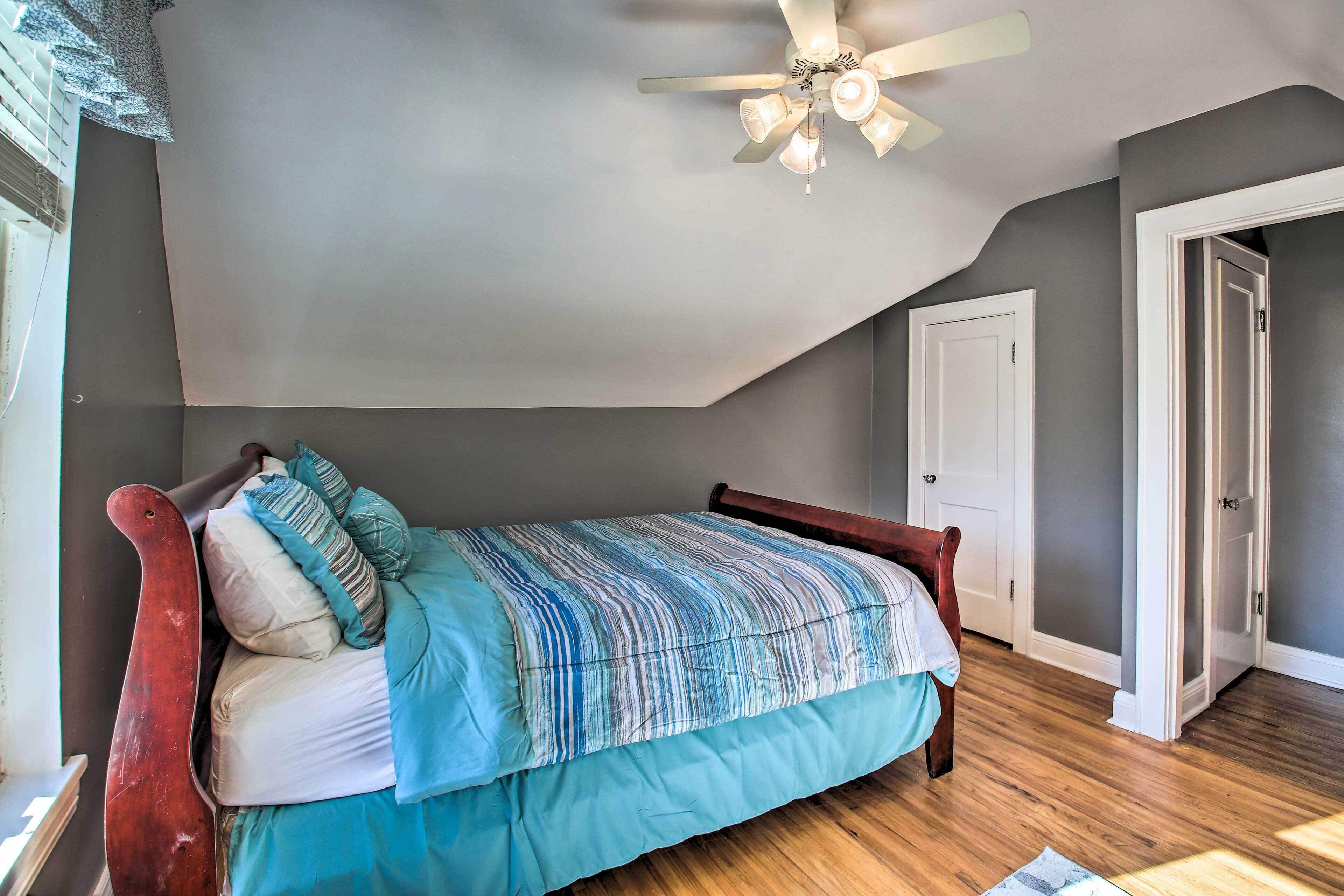 A bedroom with a wooden bed, a ceiling fan, and a door leading to another room.