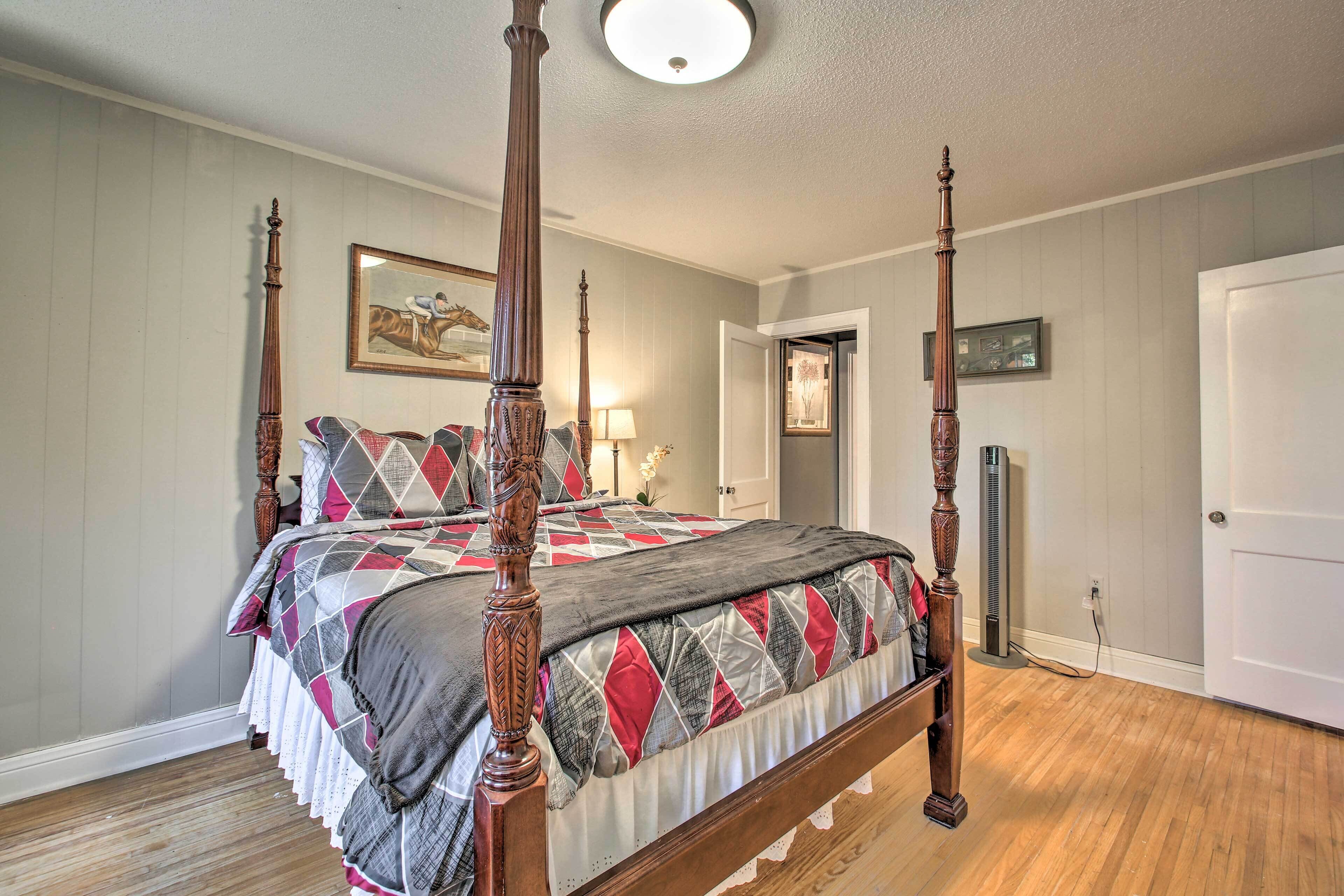 A four-poster bed with a quilt, a wooden floor, and a door in the background.