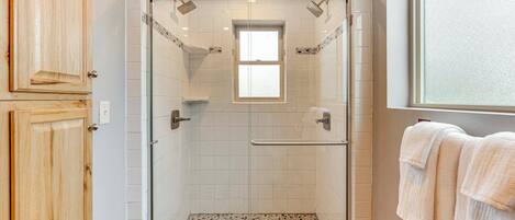 Een douche met een glazen deur, een klein raam en een betegelde vloer.