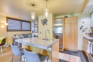 Cozinha moderna com ilha central, eletrodomésticos de aço inoxidável e área de refeições com cadeiras e mesa.