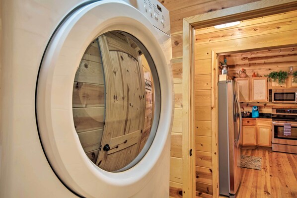 Un cuarto de lavandería con lavadora de carga frontal, gabinetes de madera, microondas y refrigerador.