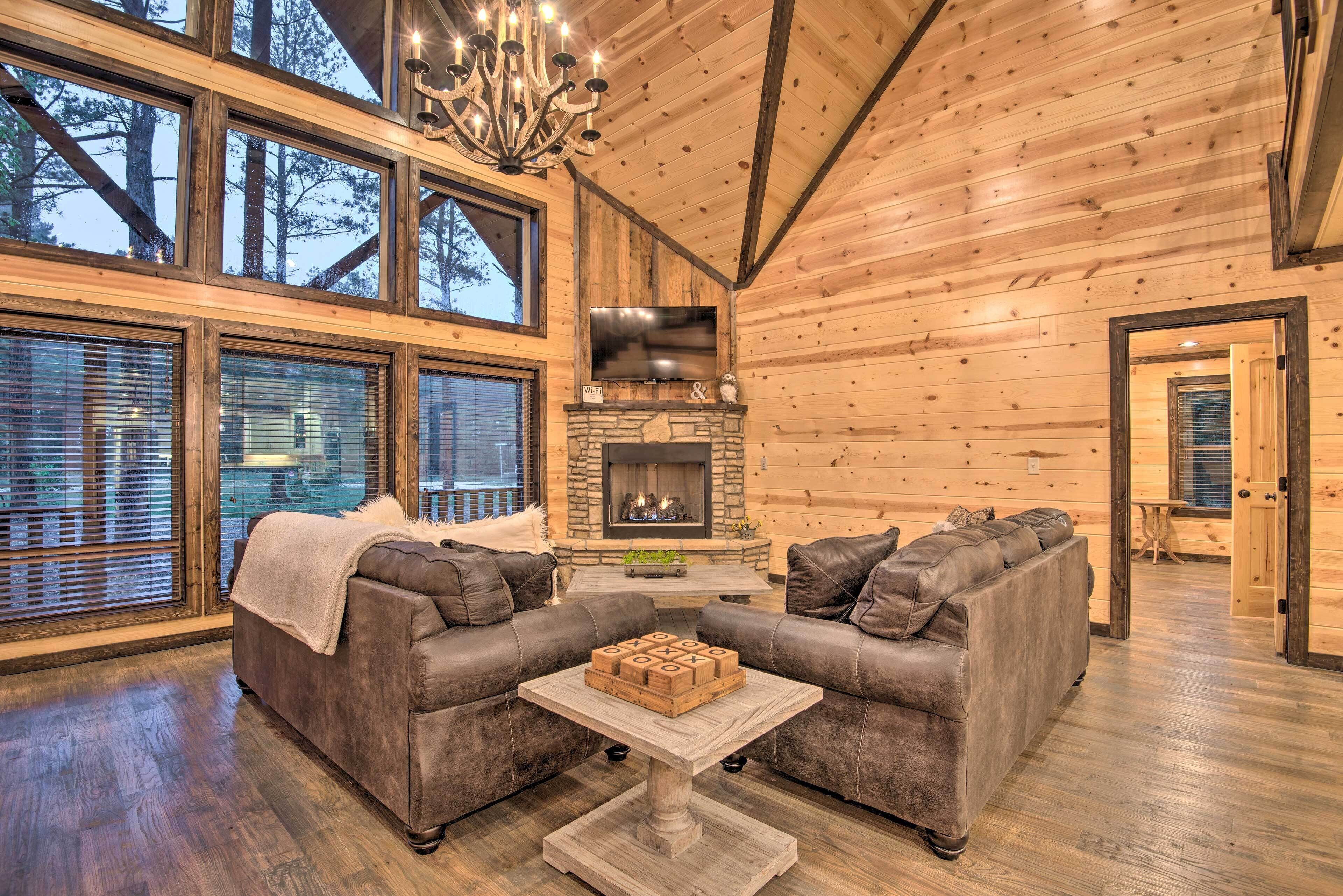 Acogedor interior de cabaña de madera con dos sofás, una chimenea y ventanas amplias.